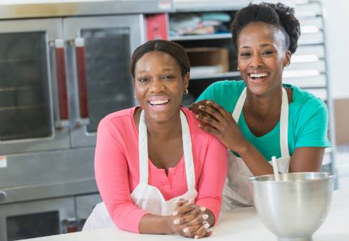 Two individuals in aprons smiling at the camera in a kitchen