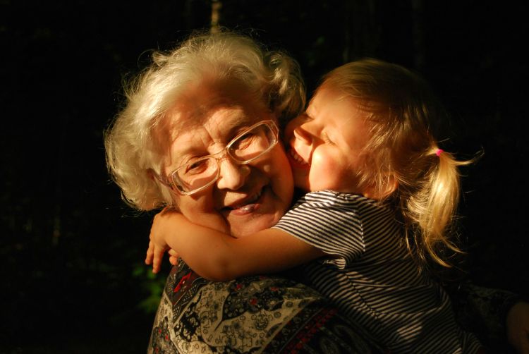 A granddaughter hugs her grandmother, both look happy.
