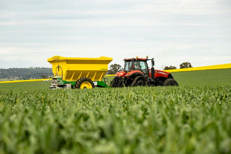red tractor pulling yellow wagon across a green field.