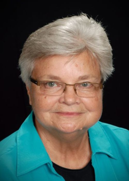 A headshot of a person wearing a teal blazer.