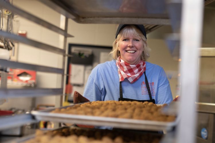 A school food program manager smiles while placing a tray of food on the speed rack