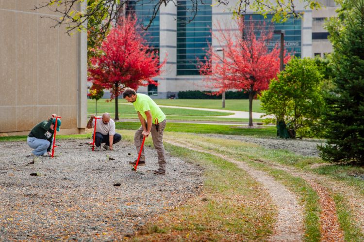 three people planting a pollinator garden along the side of a building
