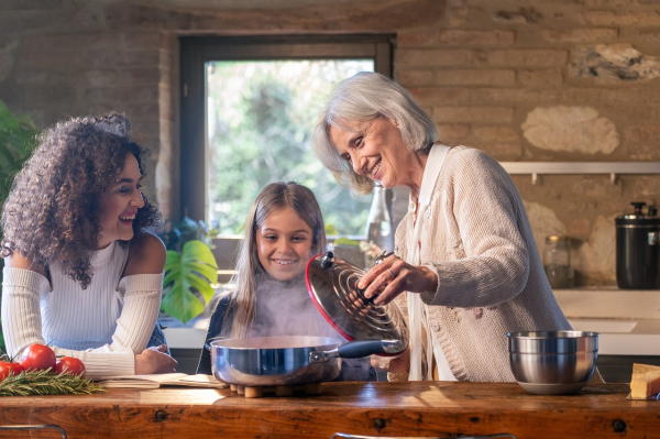 A photo of a family that includes a mother, a daughter, and a grandmother cooking dinner together.