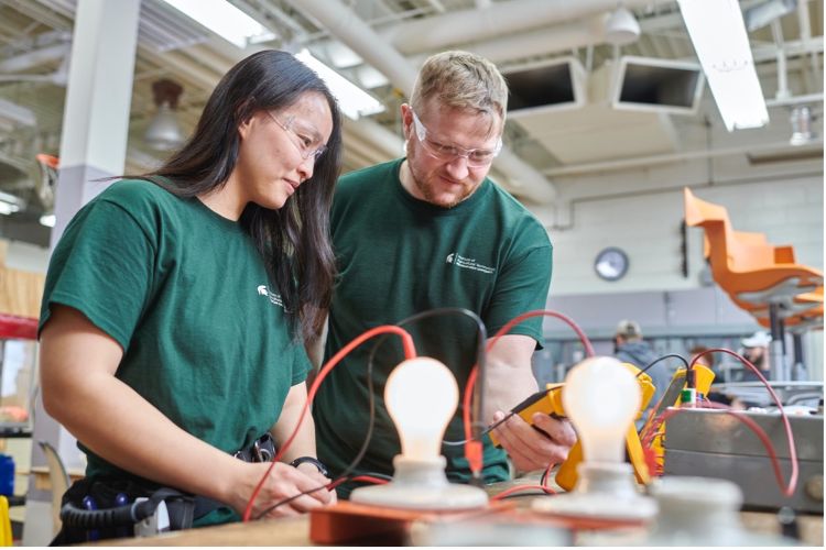 Two people looking at a yellow box power meter with a lightbulb