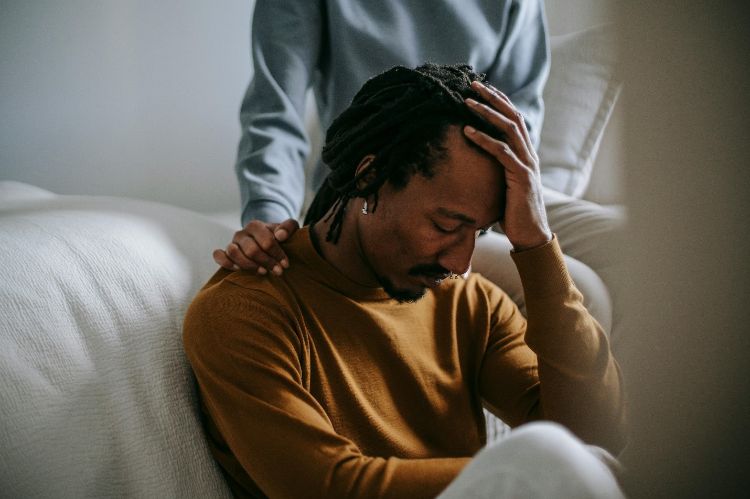 A person comforting another distressed person on a couch.