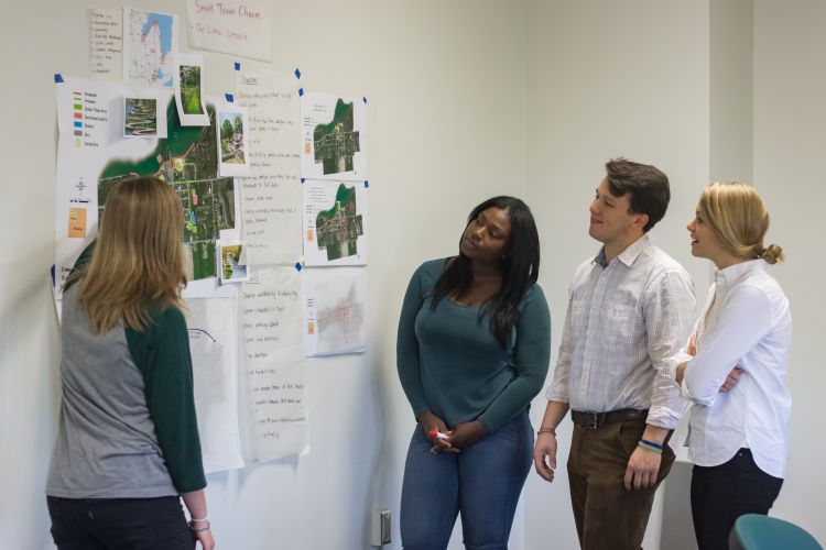 Student presenting poster to three other students.