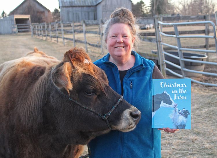 A woman with a blue vest on holding up a book in one hand and holding the halter of a Jersey cow in the other.