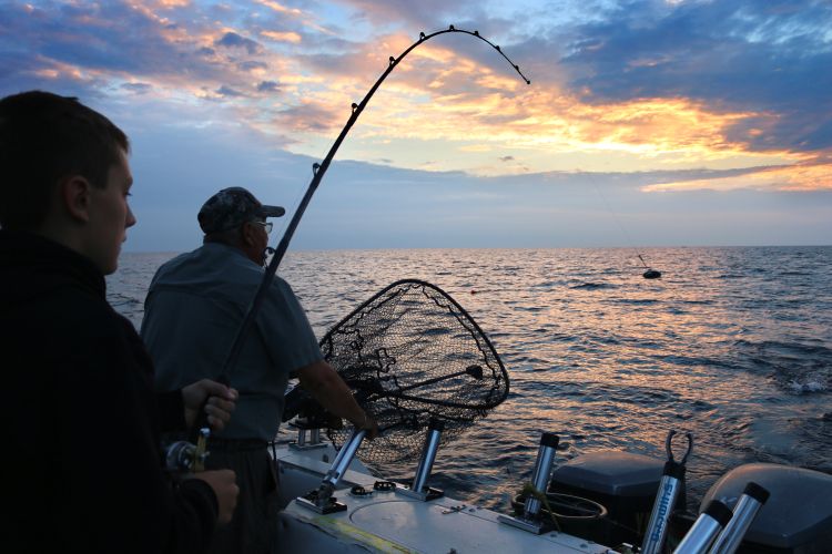 Two people are fishing off the end of a charter boat, looking out over the water.