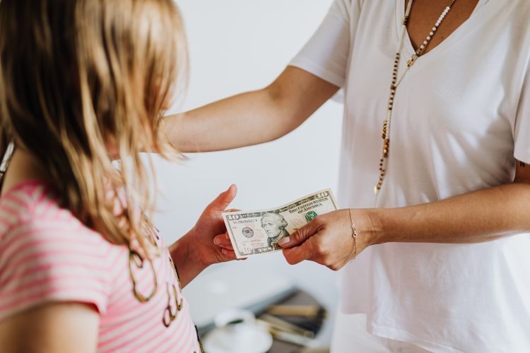 An adult handing over a ten dollar bill to a child.