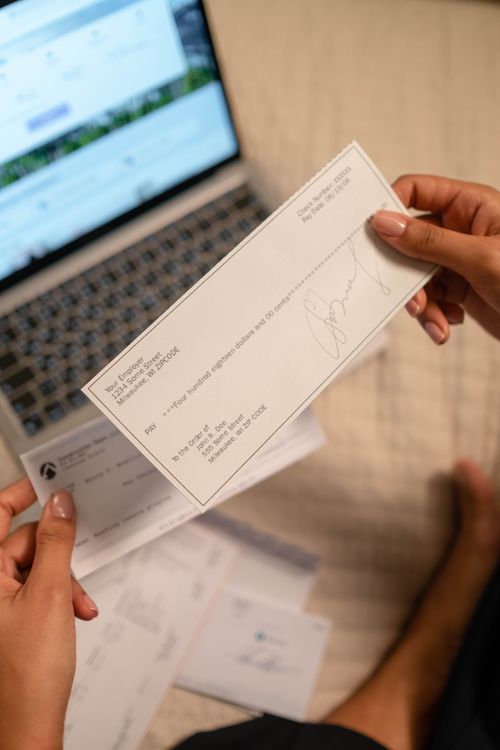 Hands holding a check with a computer in the background.
