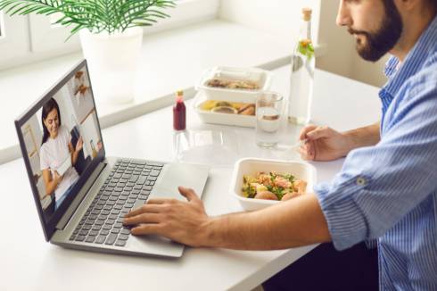 a person sitting at a table with a laptop and a bowl of food