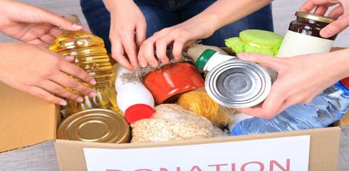 Several hands placing canned food items into a box.