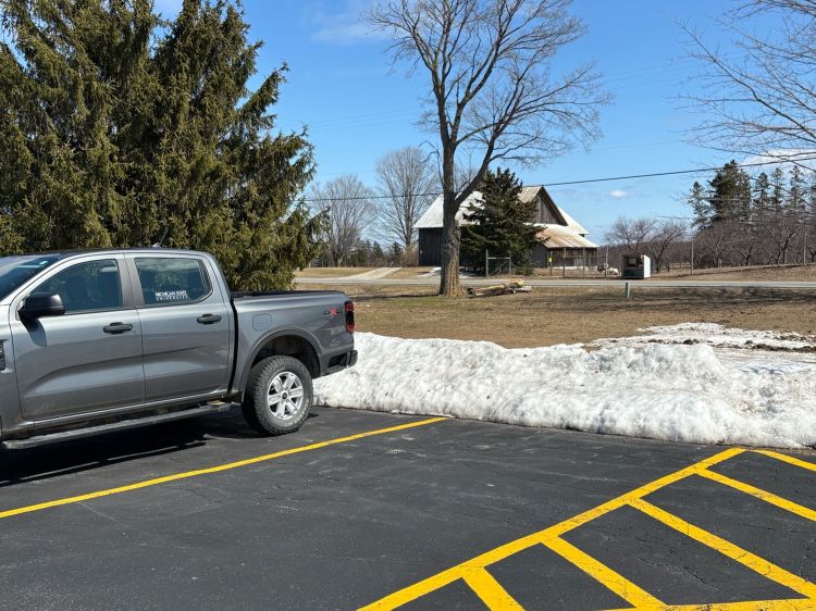 A truck parked in a parking lot with piles of snow around the edge of the parking lot.