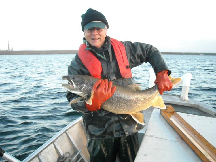 Man on a boat on the water is seen holding a large fish he has just caught. It takes both hands to hold the fish.