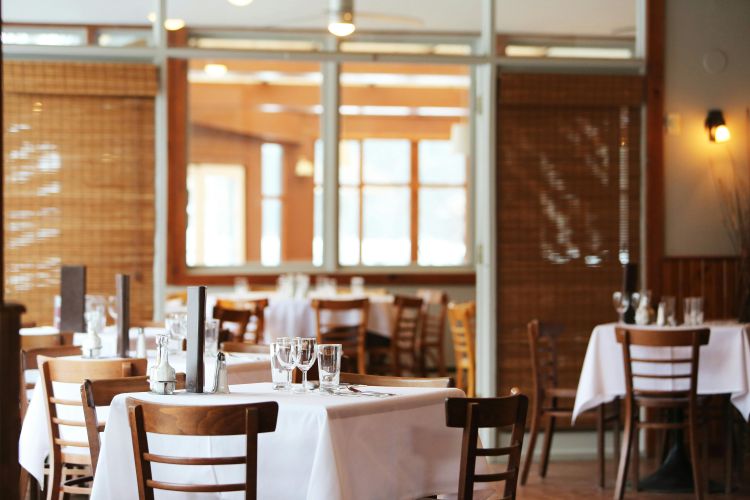 A photo of an empty restaurant with wine and water glasses on the tables.