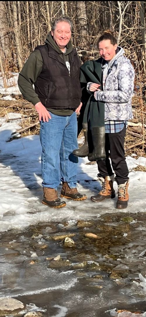 A man and a young woman stand together facing the camera