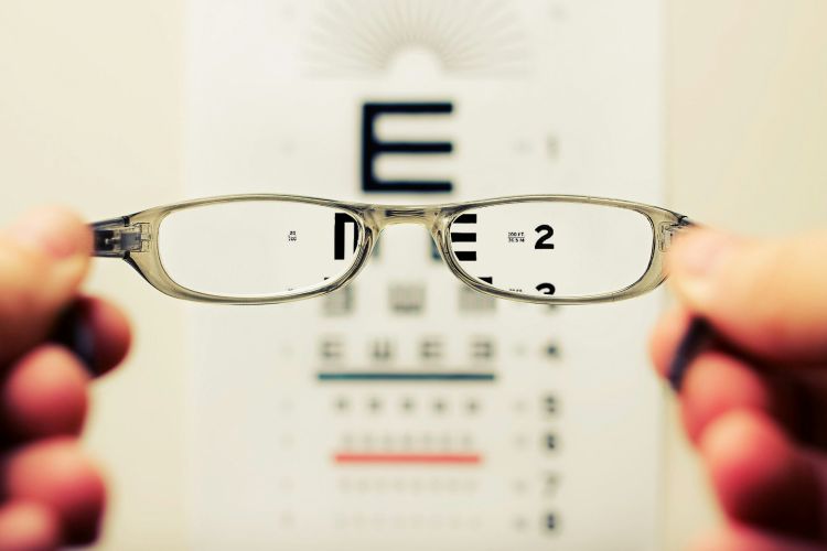 Hands holding eye glasses and looking at an eye chart.