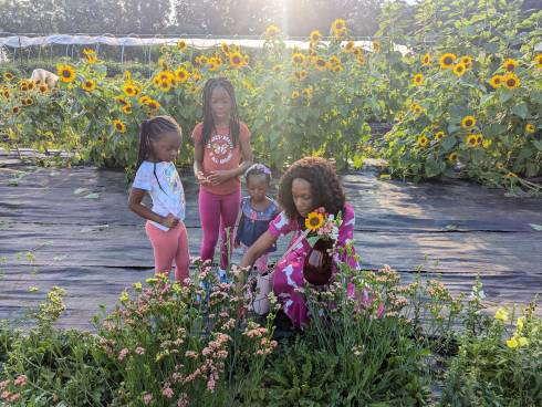 three girls and their mother harvesting flowers and placing them in a red glass vase