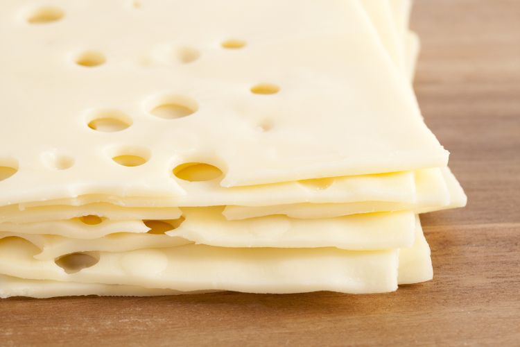 stack of cream colored cheese with holes in it on a brown surface