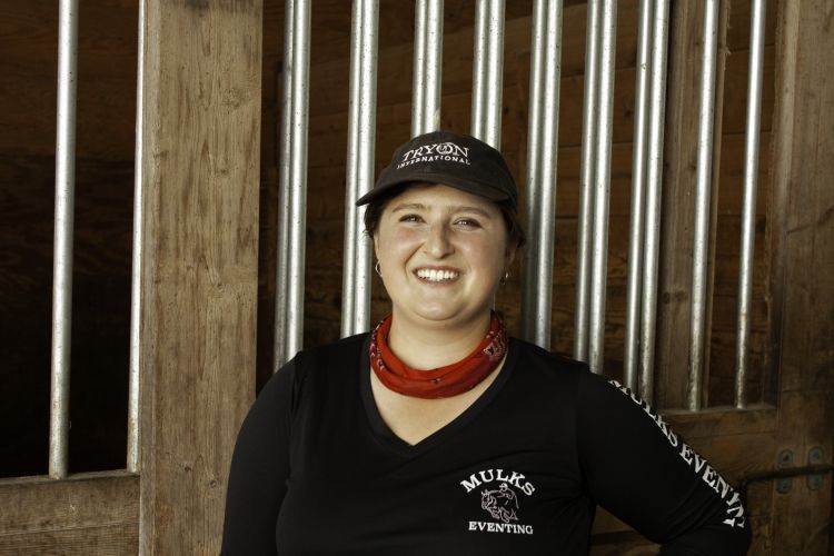 Student smiling in the camera with a hat and wood background.