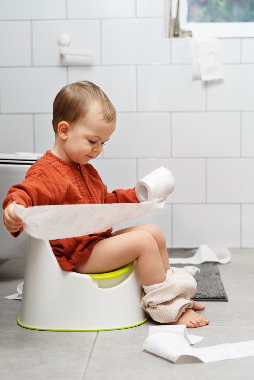 A boy sitting on a small potty with toilet paper.