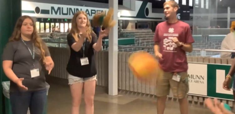 A group of youth standing in a circle tossing a ball.