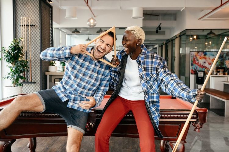 Two people laughing while playing pool.