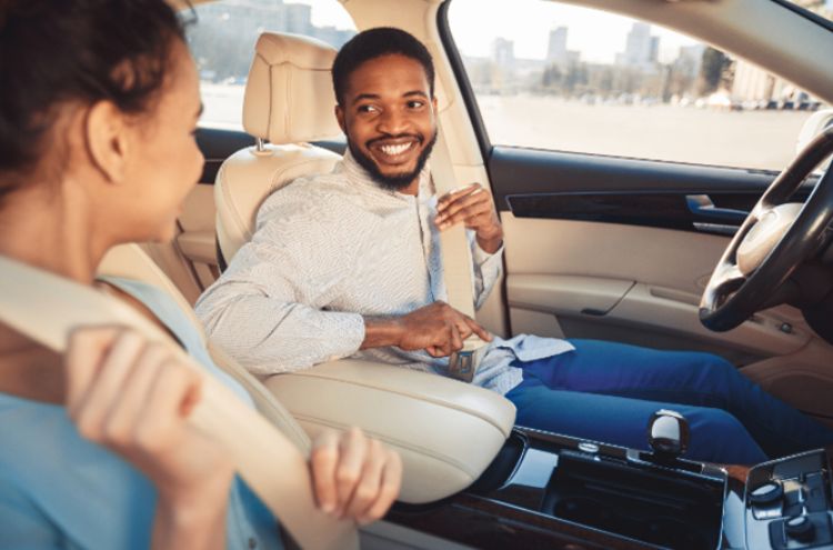 Two people sitting in a car wearing seat belts.