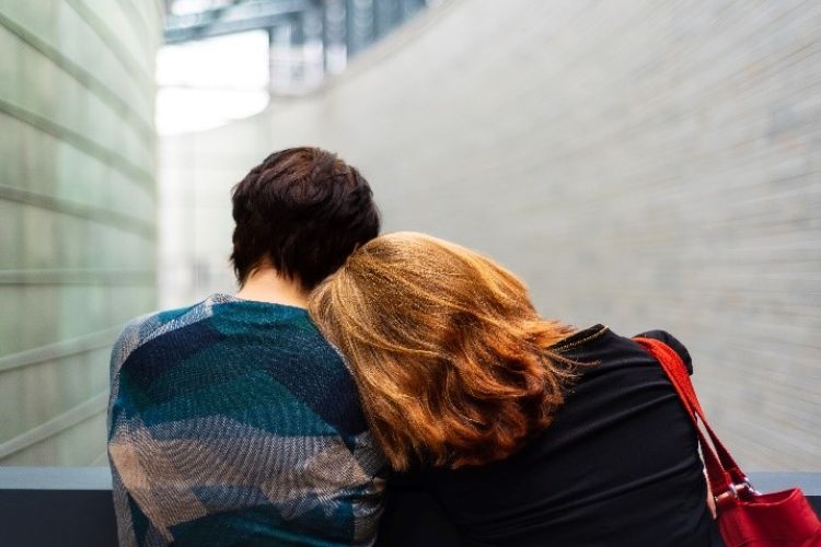 A blond person leaning their head on the shoulder of another person with short brown hair.