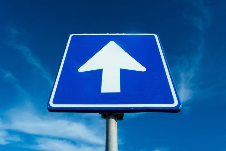 A blue road sign with an arrow pointing up into a blue sky.