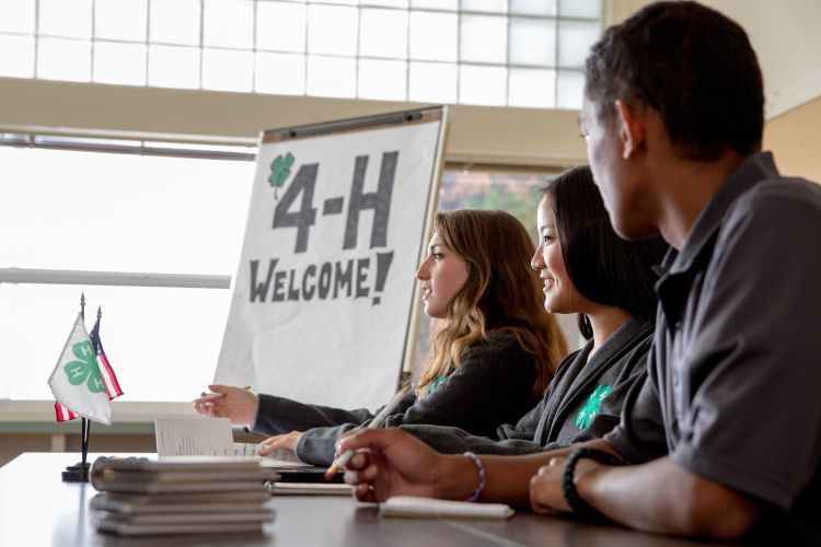 Youth sitting at a table with a sign behind them saying 