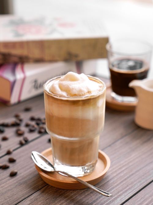 A photo of a coconut coffee in a glass on a table with a spoon next to it.