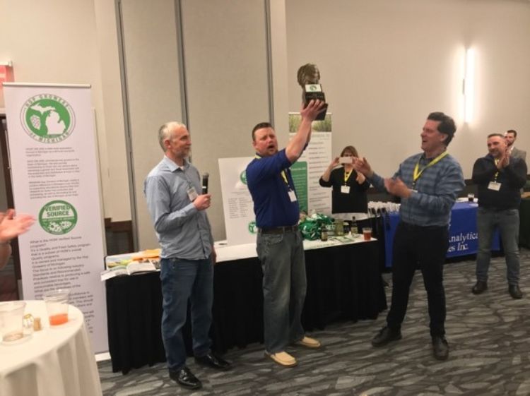 Two guys standing around a guy holding a trophy