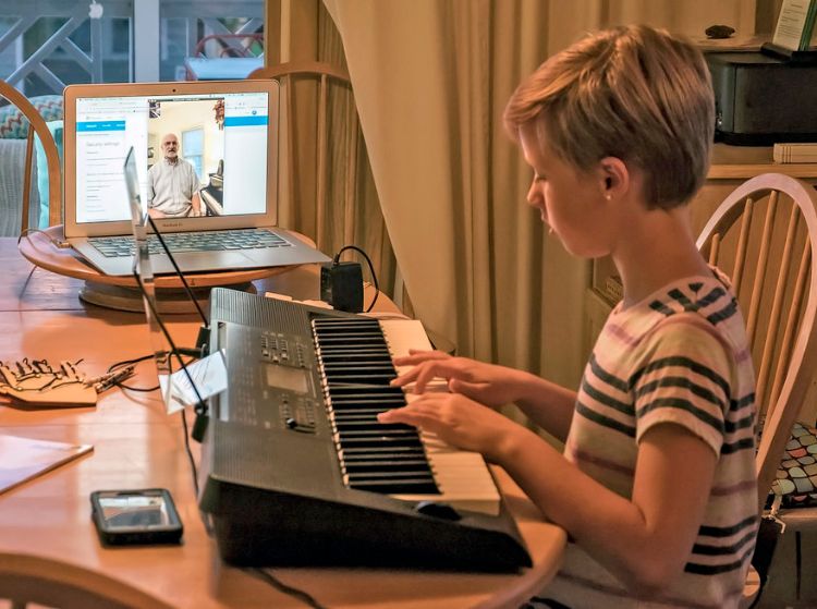 Girl playing the piano with laptop open in next to her