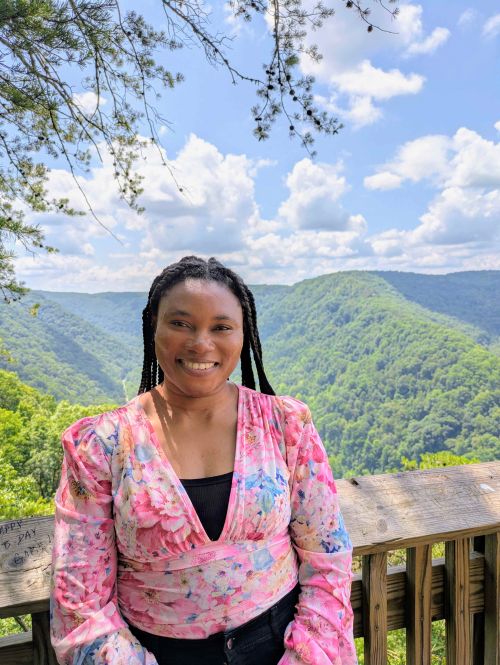 MSU Forestry Master's student, Esther Tonade, posting for a picture with mountains in the background and a cloudy blue sky.