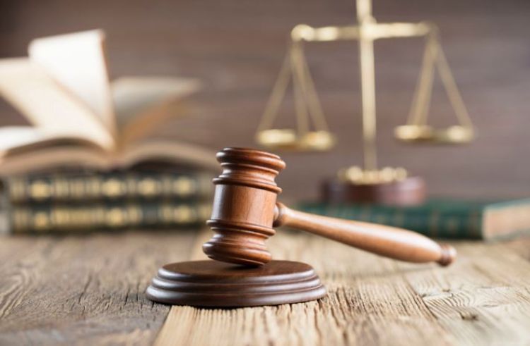 Wood gavel in foreground with scales of justice and books in background of photo.