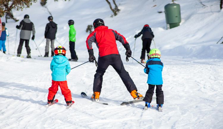 Two kids on skis being pulled by ski poles by an adult on skis.
