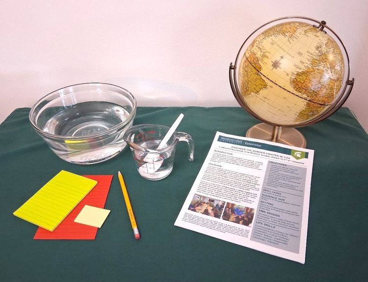 A table with a bowl of water, measure cup with water, a globe, lesson plan, pencil and some papers.