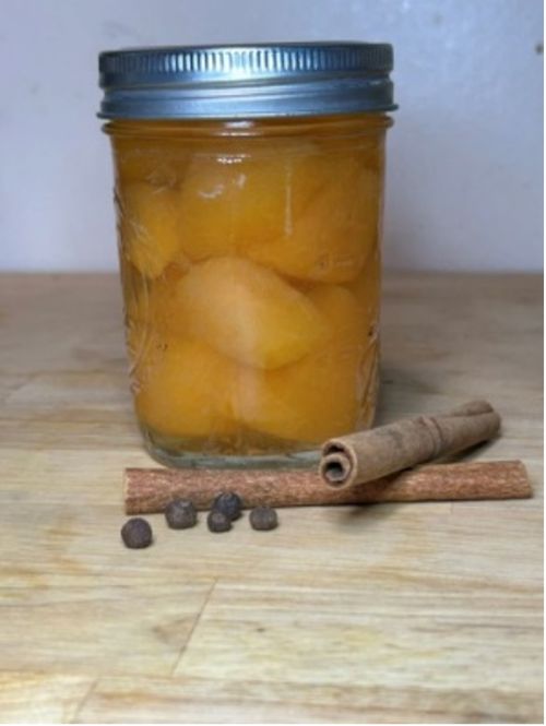 Spicy Melon Pickles  in a jar sitting next to cloves and cinnamon sticks.