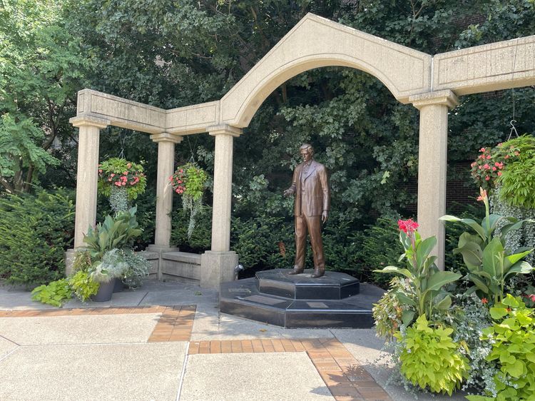 A statue under a stone archway in gardens.