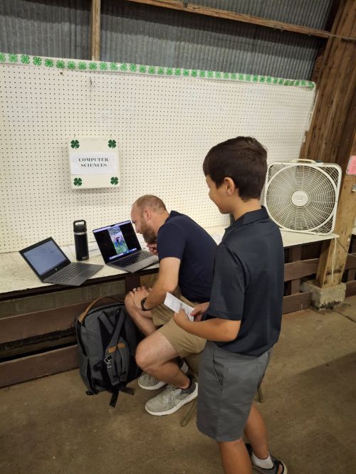 A young person talking to an adult as they work on a computer.