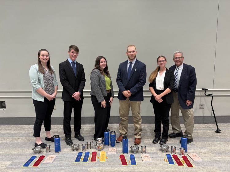 Four individuals and two coaches standing in front of their ribbons and trophies.
