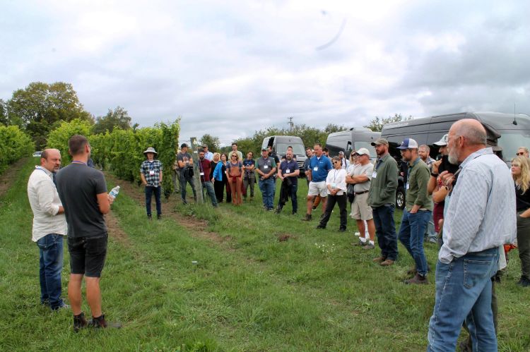 A group of people standing in a semi-circle in a field watching two presenters.