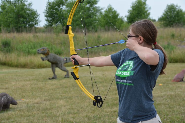A young lady in a grey shirt pulls back a yellow bow.