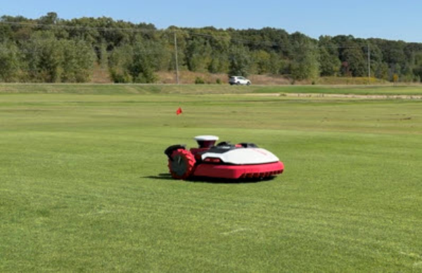 A white and red mower in a green field with a line of trees in the background.