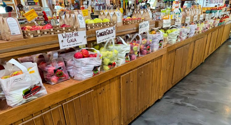 Assorted apples for sale on a wooden shelf.