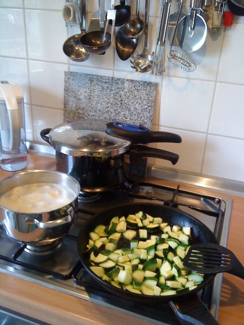 Stove with pressure cooker, zucchini, and boiling corn in pot.