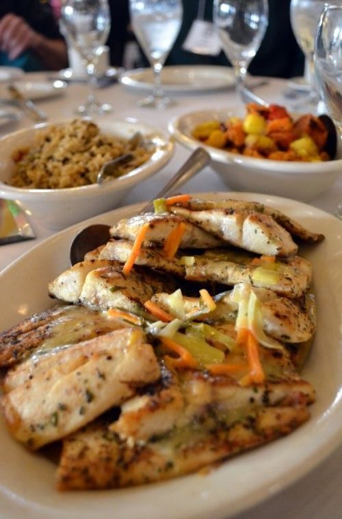 A dinner setting with a fish meal plated on a table, showing a whitefish dinner with full dinner setting.