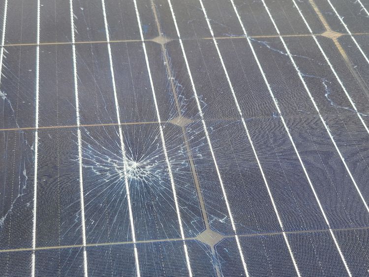 photo of a dark gray solar panel damaged by a rock