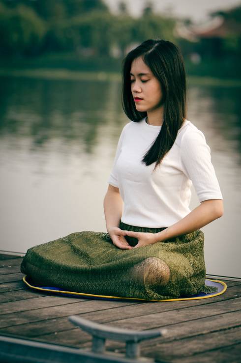 An Asian woman sitting on a dock meditating.